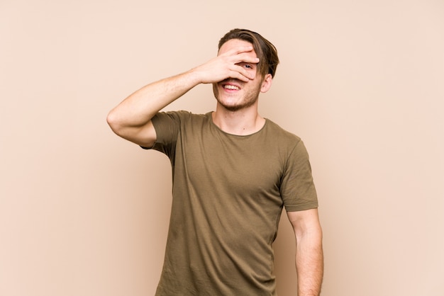 Young caucasian man posing isolated blink at through fingers, embarrassed covering face.