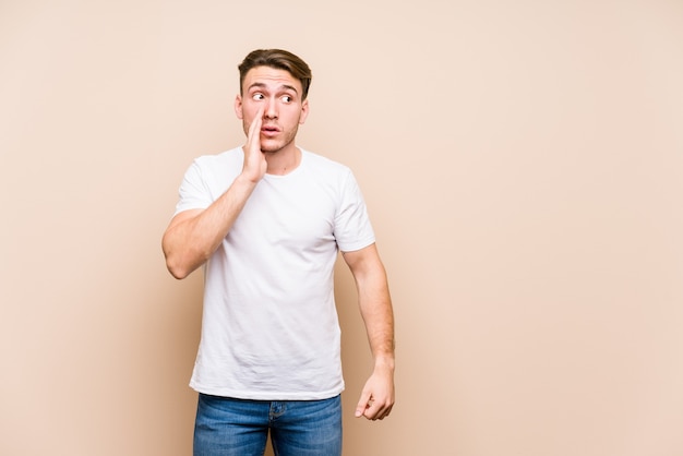 Young caucasian man posing isolated is saying a secret hot braking news and looking aside