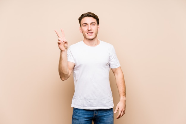 Young caucasian man posing isolated joyful and carefree showing a peace symbol with fingers.