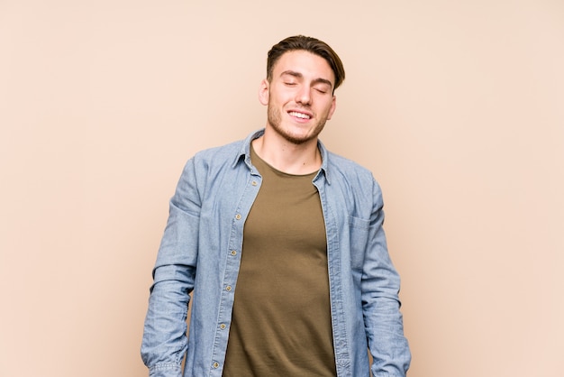 Young caucasian man posing laughs and closes eyes, feels relaxed and happy.