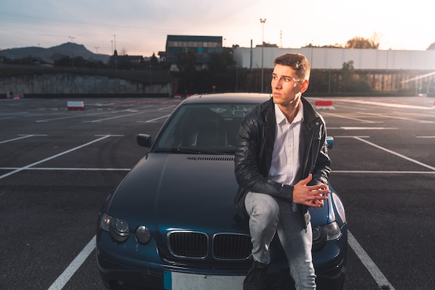 Giovane uomo caucasico in posa in un parcheggio con un'auto sportiva