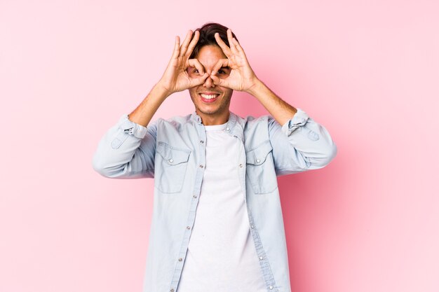 Young caucasian man posing in a pink isolated showing okay sign over eyes