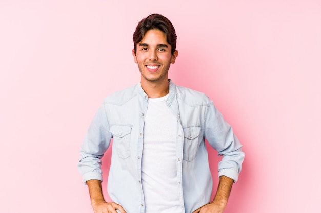 Foto giovane uomo caucasico che posa in una parete rosa fiduciosa tenendo le mani sui fianchi.