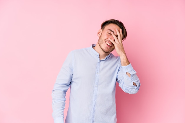 Young caucasian man posing in a pink wall isolated blink at the camera through fingers, embarrassed covering face.