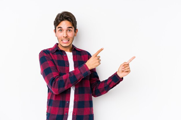 Young caucasian man posing in a pink wall isolated shocked pointing with index fingers to a copy space.