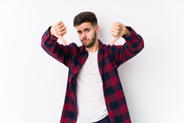 Young caucasian man posing in a white background isolated showing thumb down and expressing dislike.