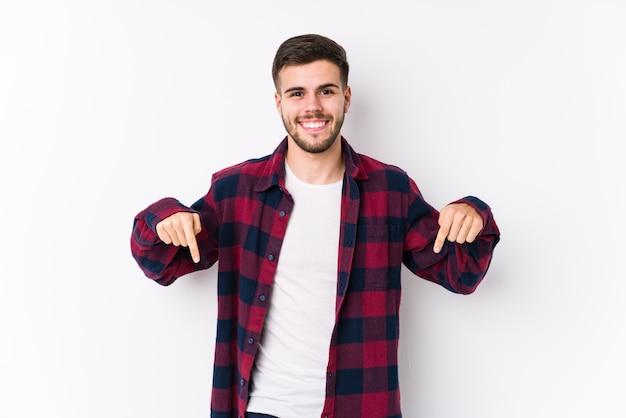 Young caucasian man posing in a white wall isolated points down with fingers, positive feeling.