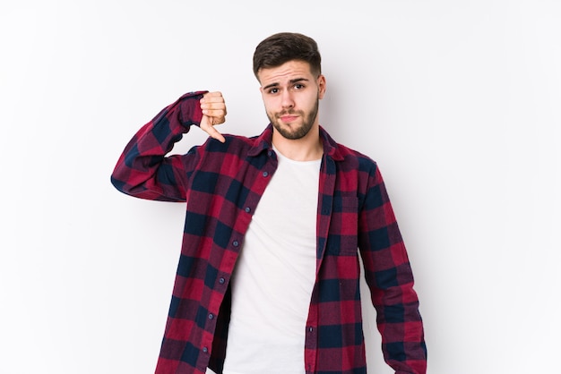 Young caucasian man posing in a white wall showing a dislike gesture, thumbs down