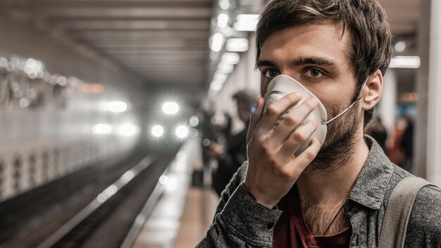 Giovane uomo caucasico in maschera di protezione contro il virus alla stazione della metropolitana pubblica in attesa del treno