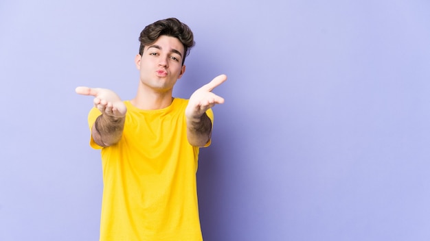 Young caucasian man on purple folding lips and holding palms to send air kiss.