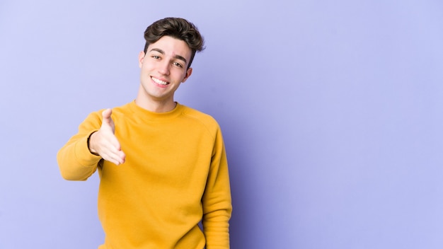 Young caucasian man on purple stretching hand in greeting gesture.