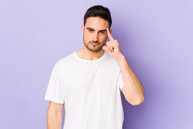 Young caucasian man on purple wall pointing temple with finger, thinking, focused on a task.