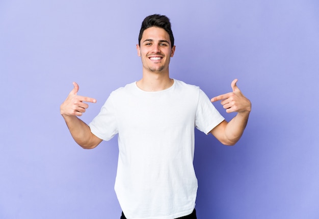 Young caucasian man on purple wall points down with fingers