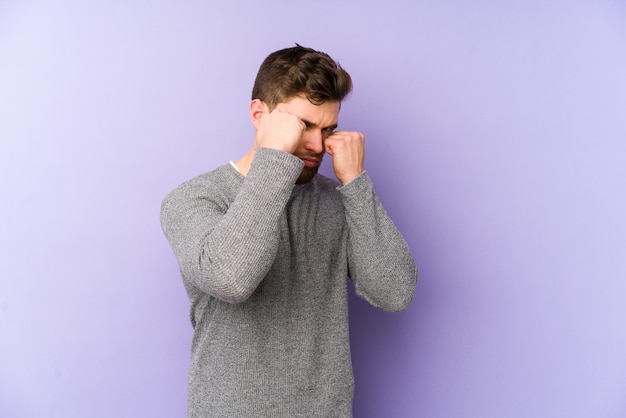 Young caucasian man on purple wall throwing a punch, anger, fighting due to an argument, boxing.