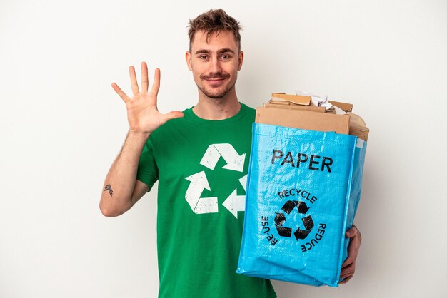 Young caucasian man recycled paper isolated on white background smiling cheerful showing number five with fingers.