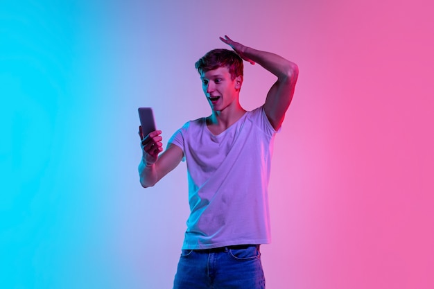 Il giovane uomo caucasico sta saltando in alto sullo sfondo dello studio blu-rosa sfumato alla luce al neon