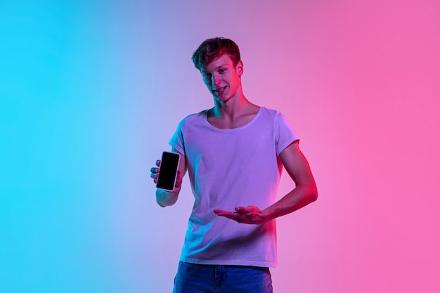 ネオンの光のグラデーションの青ピンクのスタジオの背景に若い白人男性の肖像画