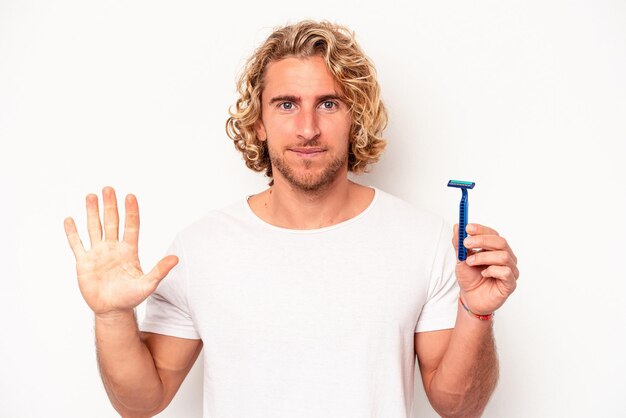 Young caucasian man shaving his beard isolated on white background smiling cheerful showing number five with fingers.