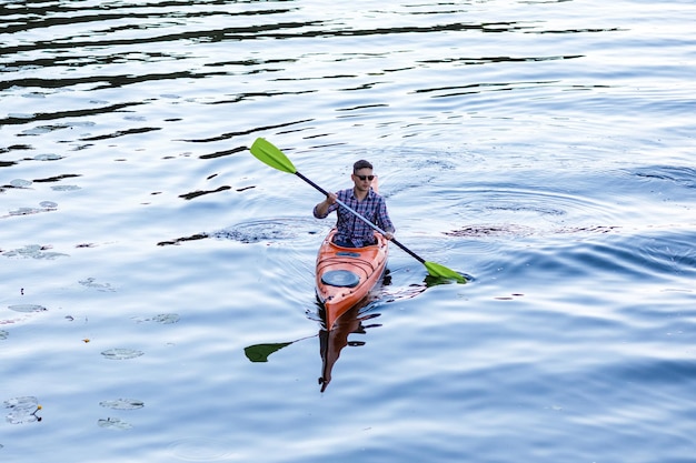 Un giovane uomo caucasico si siede in un kayak e pagaie il concetto di intrattenimento in acqua