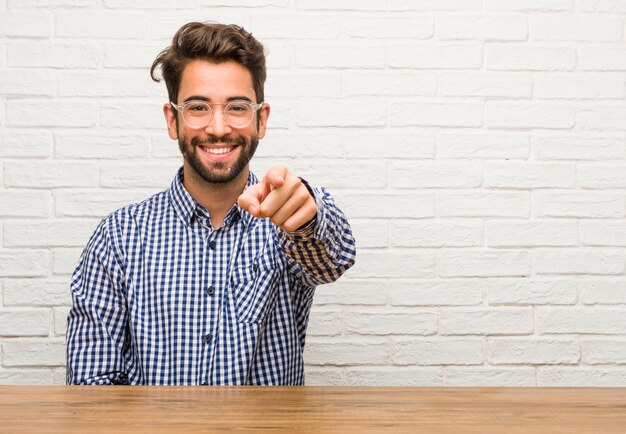 Young caucasian man sitting cheerful and smiling pointing to the front