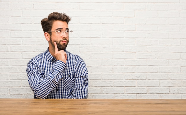 Young caucasian man sitting doubting and confused, thinking of an idea or worried about something