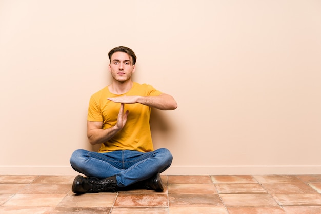 Young caucasian man sitting on the floor isolated showing a timeout gesture.