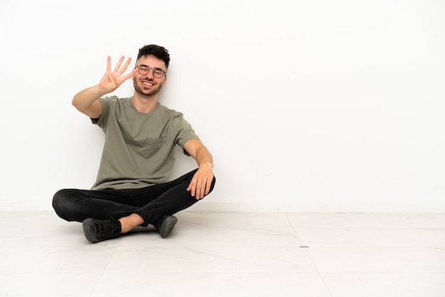 Young caucasian man sitting on the floor isolated on white background happy and counting four with fingers