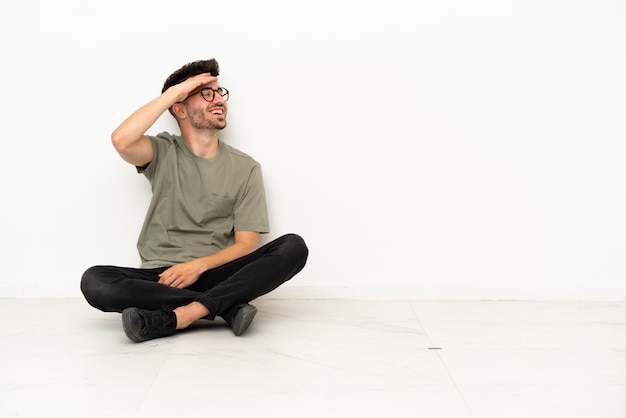 Молодой кавказский человек, сидящий на полу, изолированном на белом фоне, что-то понял и намеревается найти решение