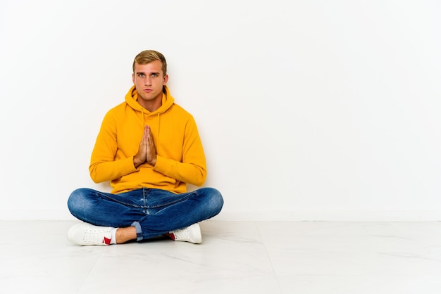 Photo young caucasian man sitting on the floor praying, showing devotion, religious person looking for divine inspiration.