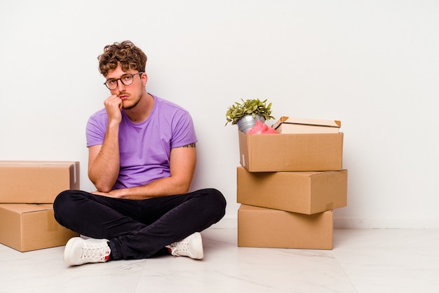 Young caucasian man sitting on the floor ready for moving isolated on white background who is bored, fatigued and need a relax day.