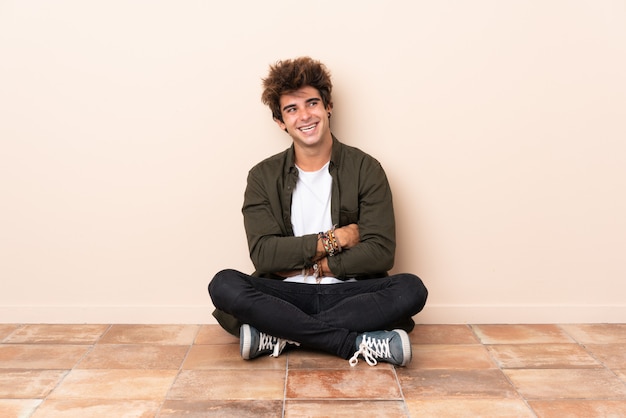 Photo young caucasian man sitting on the floor with arms crossed and happy