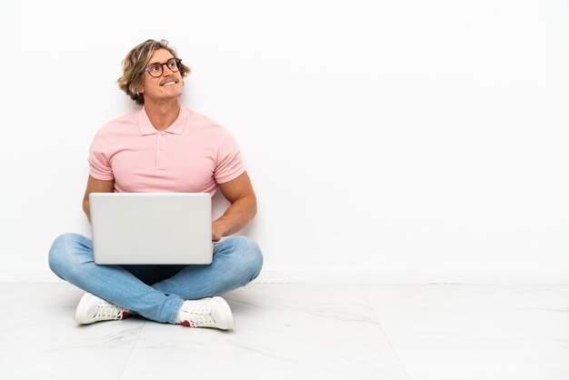 Young caucasian man sitting on the floor with his laptop isolated