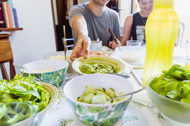 Giovane uomo caucasico seduto accanto alla sua ragazza che mangia prendendo con la mano una ciotola dal tavolo