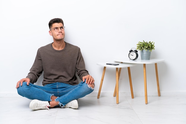 Young caucasian man sitting in his home isolated on white background and looking up