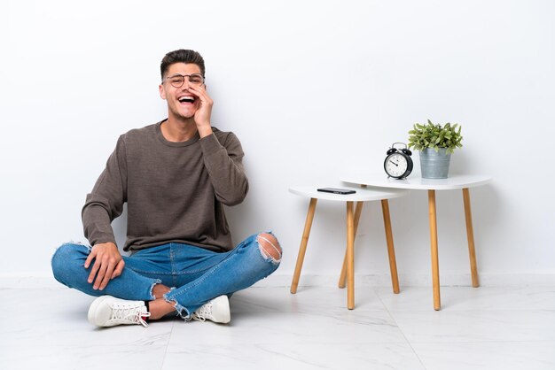 Young caucasian man sitting in his home isolated on white background shouting with mouth wide open