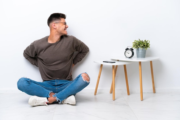 Photo young caucasian man sitting in his home isolated on white background suffering from backache for having made an effort