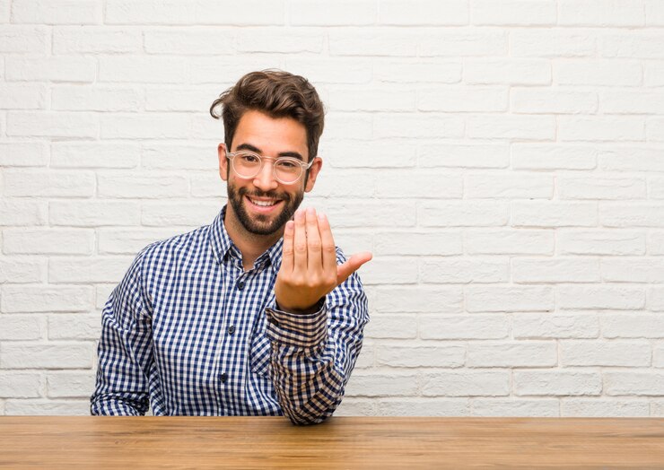 Photo young caucasian man sitting inviting to come, confident and smiling making a gesture with 