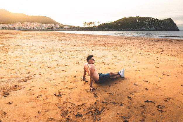 Young caucasian man sitting on the sand of a basque beach.