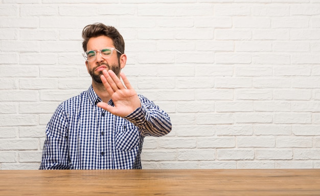 Photo young caucasian man sitting serious and determined, putting hand in front