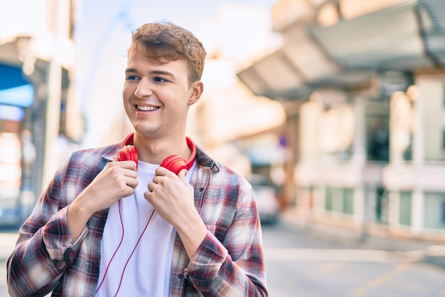 Foto giovane uomo caucasico che sorride felice usando le cuffie in città