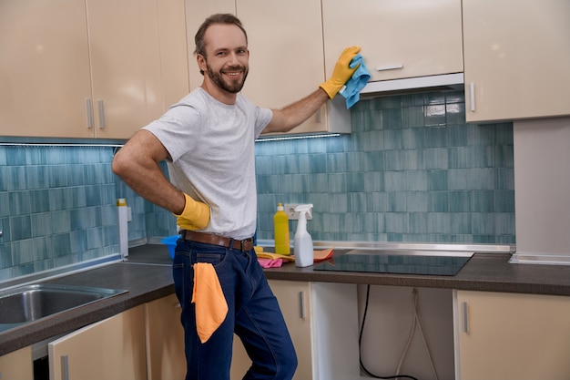 Young caucasian man smiling while cleaning kitchen furniture