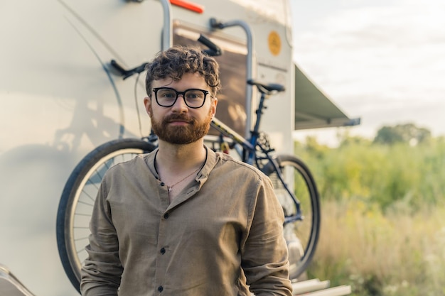 Young Caucasian man standing in front of the recreation vehicle with bicycle attached