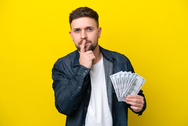 Young caucasian man taking a lot of money isolated on yellow background having doubts while looking up