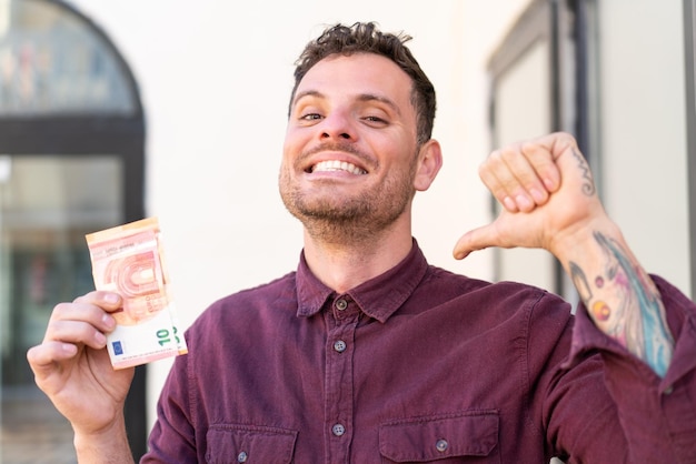 young caucasian man taking a lot of money at outdoors proud and selfsatisfied