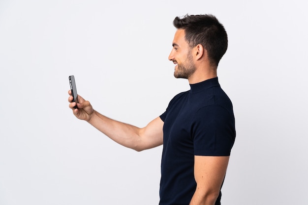 Young caucasian man using mobile phone isolated on white background with happy expression