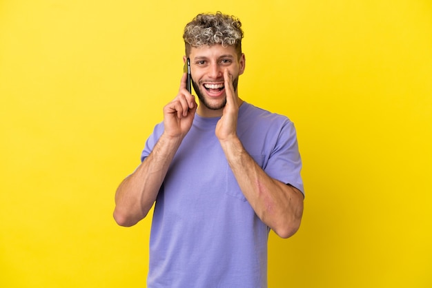 Young caucasian man using mobile phone isolated on yellow background shouting with mouth wide open