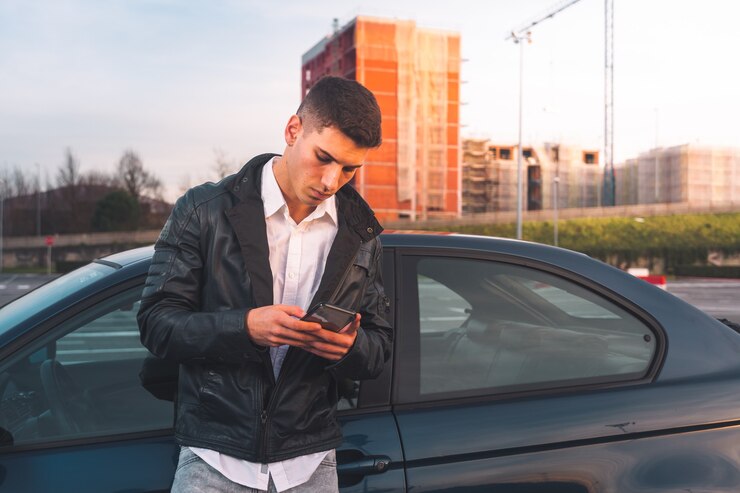 後ろにスポーツカーとスマートフォンを使用して若い白人男性