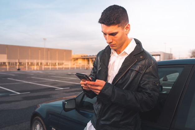 Giovane uomo caucasico utilizzando uno smartphone con un'auto sportiva dietro