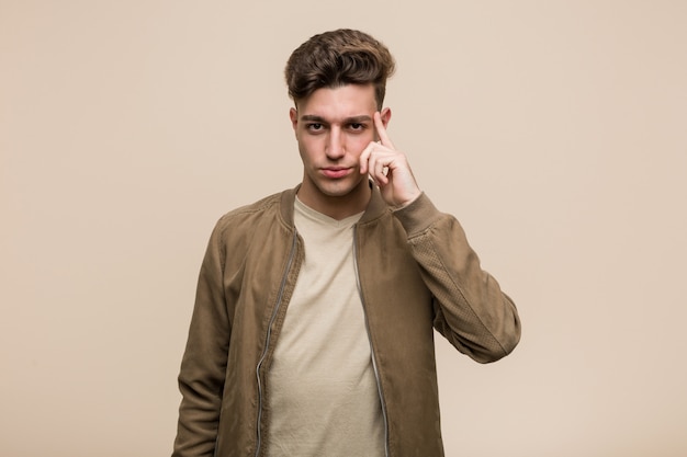 Young caucasian man wearing a brown jacket pointing temple with finger, thinking, focused on a task.