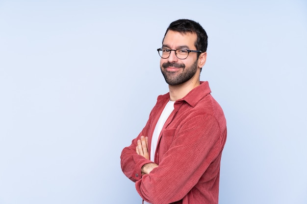 Young caucasian man wearing corduroy jacket over blue wall with arms crossed and looking forward